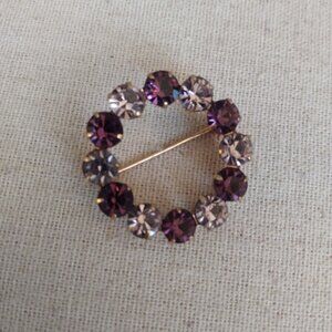 Gold tone circle brooch with purple and pink rhinestones.